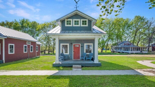 A small, single-story house with a porch, two windows, and a red door.