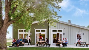 A building with outdoor seating, large windows, and a tree in front.