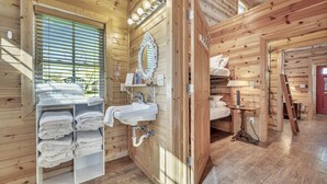 A wooden cabin interior with a bathroom, a mirror, a sink, and a bed.