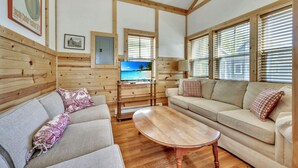 A cozy room with wooden walls, a sofa, a table, and a TV displaying a beach scene.