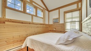 A bedroom with wooden paneling, a bed with white bedding, and a window with blinds.