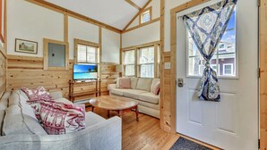 Um quarto aconchegante em estilo cabana, com sofá, televisão e porta de madeira com cortinas estampadas.