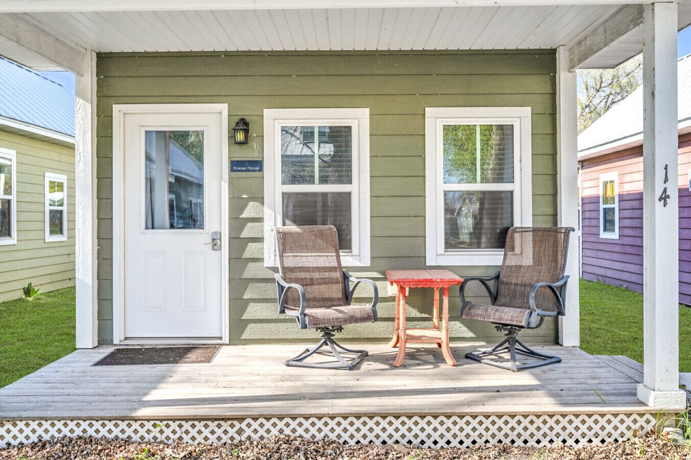 A covered porch with two chairs and a small table, a door, and a window with a sign reading 'Kreuse House.'