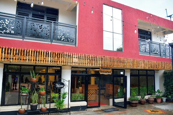 Un bâtiment à deux étages avec une façade rouge, une enseigne indiquant « Restaurant Bamboo » et des plantes en pot devant l’entrée.