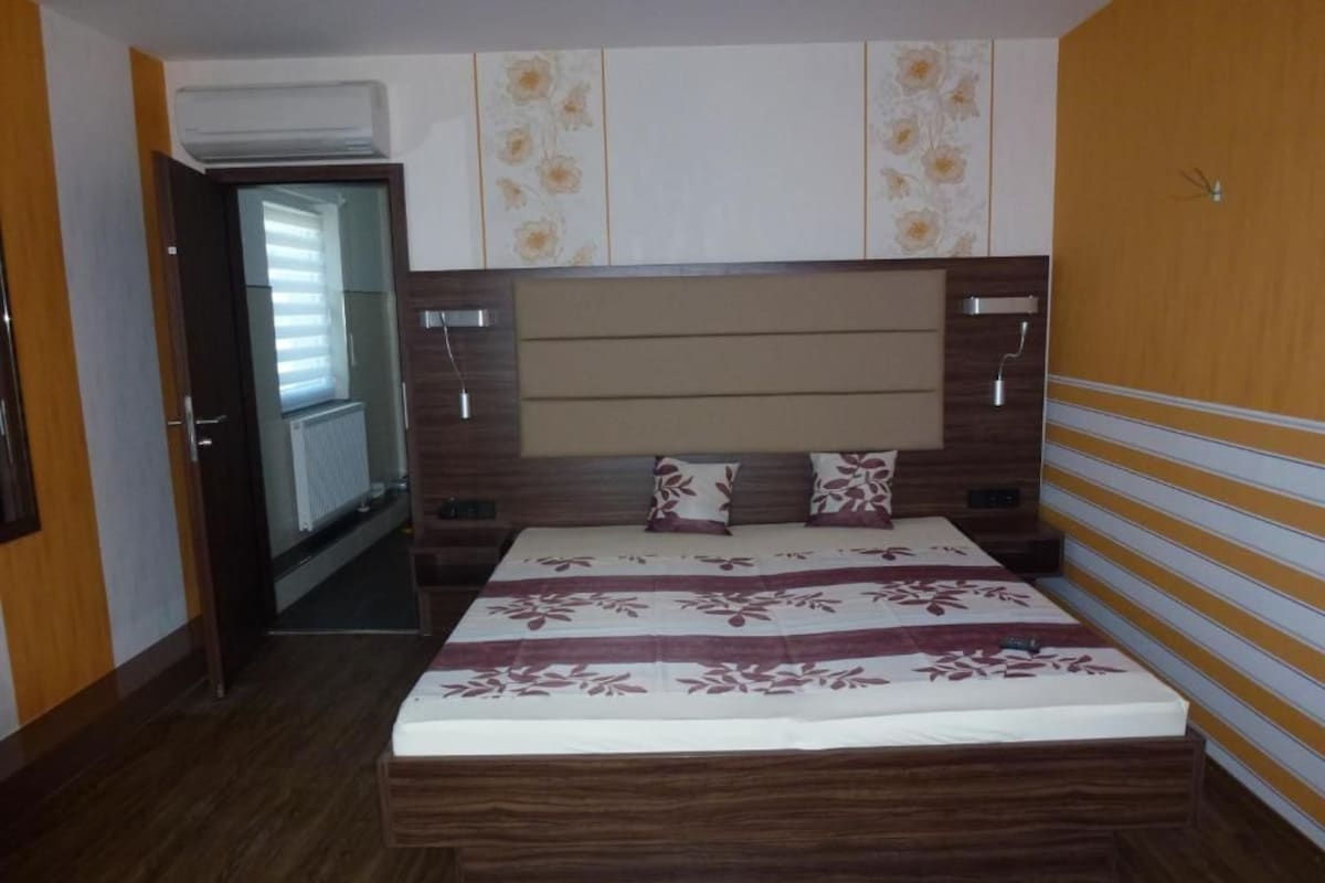 A bedroom with a wooden headboard, a bed with a floral bedspread, and a door leading to a hallway.