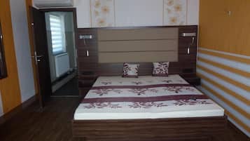 A bedroom with a wooden headboard, a bed with a floral bedspread, and a door leading to a hallway.