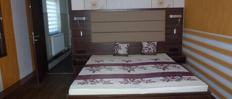 A bedroom with a wooden headboard, a bed with a floral bedspread, and a door leading to a hallway.
