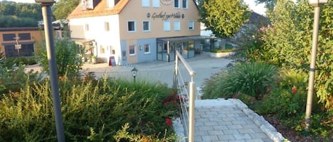 A building with a sign reading 'Gasthof zur Mühle' and a paved entrance area with a pathway leading to the building.