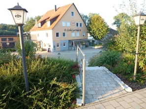 A building with a sign reading 'Gasthof zur Mühle' and a paved entrance area with a pathway leading to the building.