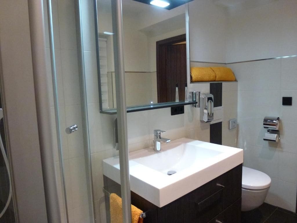 Een badkamer met een douchecabine van glas, een witte wastafel, een toilet en een handdoekrek.