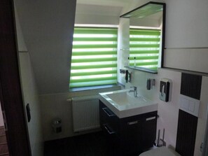 Un baño moderno con un ventanal grande, un lavamanos, un espejo y un inodoro.