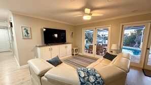 Sala de estar com sofá, TV e vista para uma piscina ao ar livre.