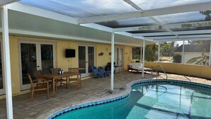 Piscina descoberta coberta com área de terraço, incluindo mesa e cadeiras, e uma televisão fixada na parede.