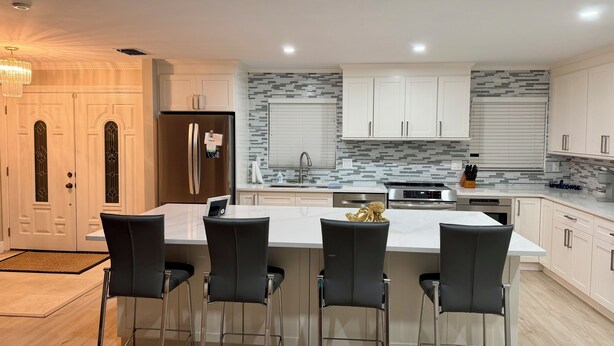 Uma cozinha moderna com uma ilha central, banquetas, eletrodomésticos de aço inoxidável e um lustre decorativo.
