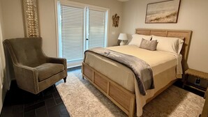 Quarto com cama, uma cadeira, um abajur e um quadro na parede.