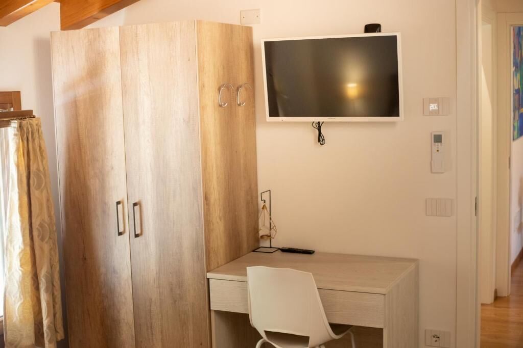 Une pièce comprenant une armoire en bois, un bureau, une chaise, un téléviseur fixé au mur et une prise de courant.