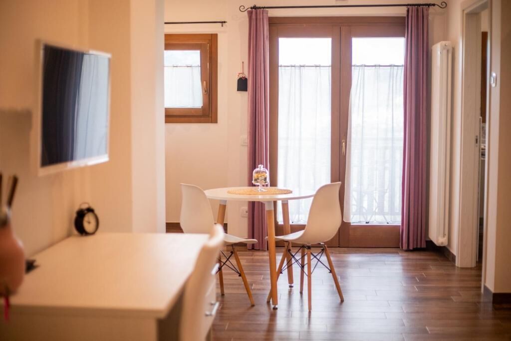A room with a round table, two chairs, a clock on the wall, and a window with curtains.