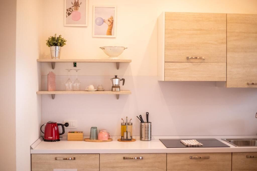 A kitchen with wooden cabinets, a countertop, a kettle, a sink, and various kitchen utensils.