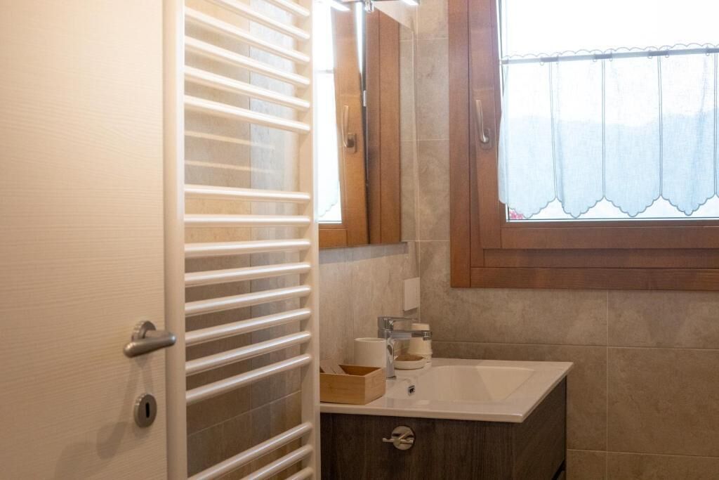 A bathroom with a wooden vanity, a white sink, a mirror, and a window with a curtain.