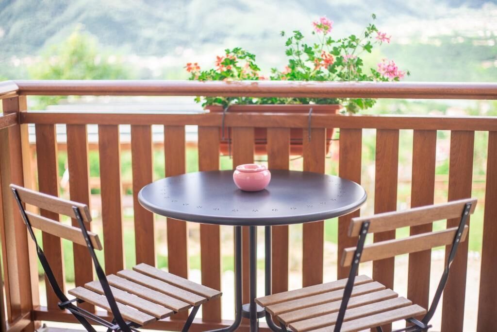 Une terrasse en bois avec une table ronde et deux chaises, un pot rose sur la table et une plante en pot avec des fleurs roses.