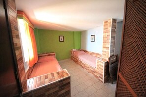 A small room with two beds, green walls, and a tiled floor.
