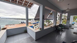Een kamer met een groot raam met uitzicht op zee, een betegelde vloer en een zithoek met stoelen.