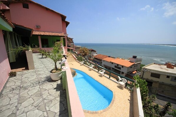 A pool area with a view of the ocean, a pink building, and a tiled patio. - Pousada do Sergio (Rio de Janeiro)