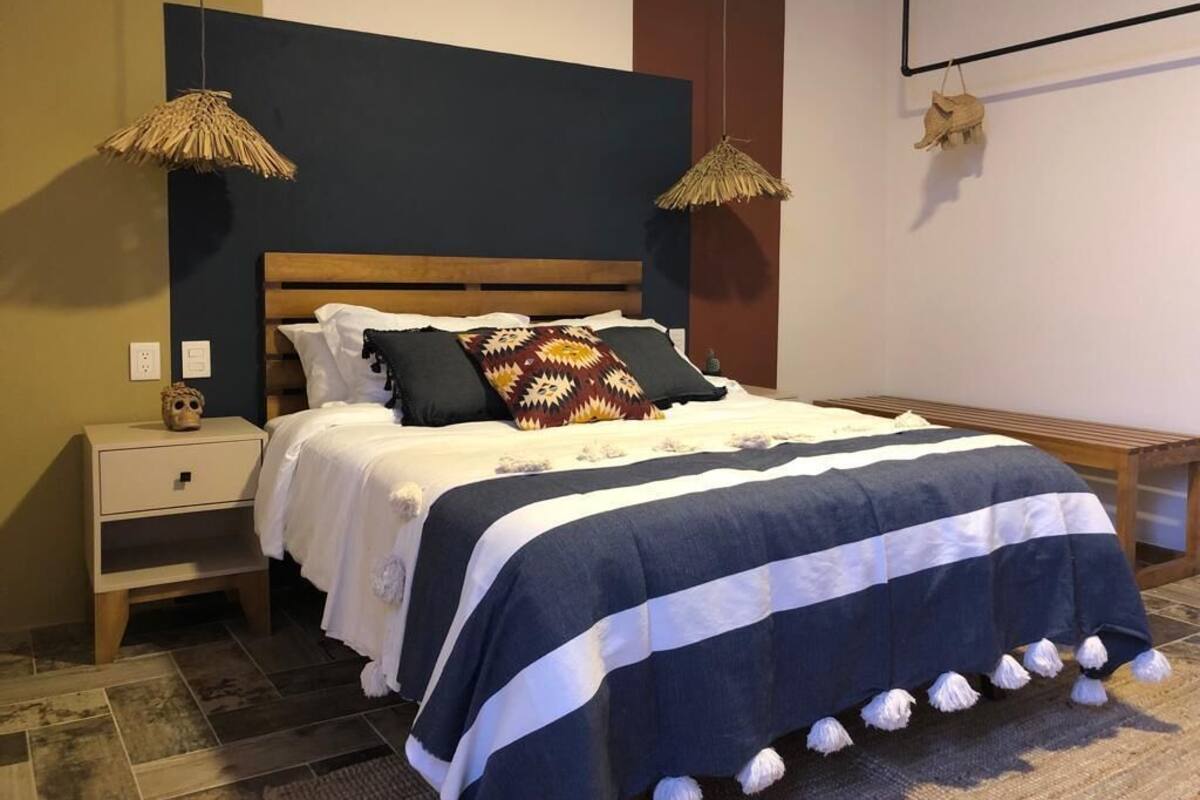 Un dormitorio con una cama de madera, un mesita de noche y dos lámparas colgantes.