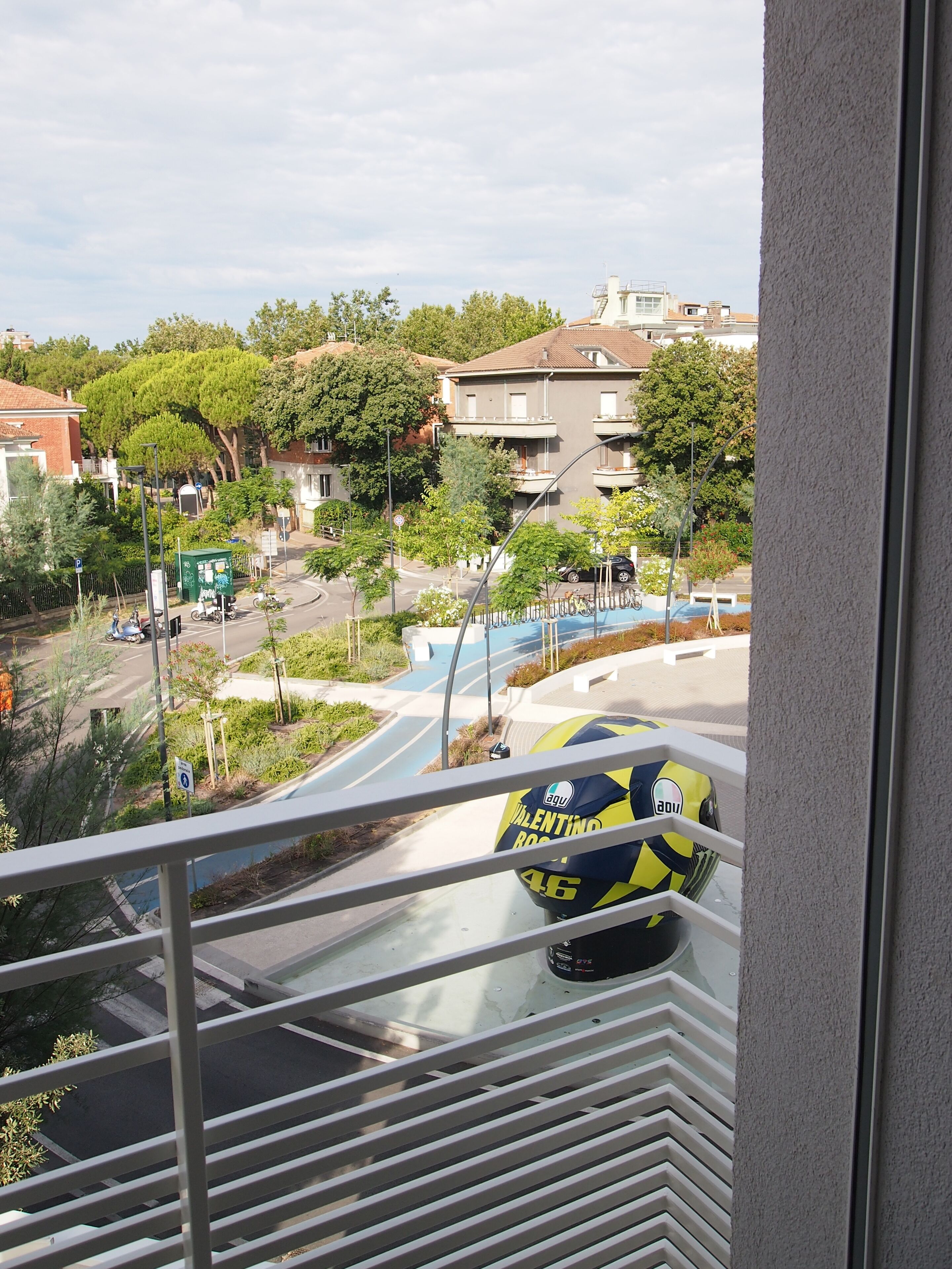 A view from a window overlooking a street with a yellow and black sports ball, a residential area with houses, and a clear sky.