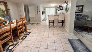 A dining area with a wooden table and chairs, a kitchen with a bar, and a living area with a couch. - 2-bedroom house w/pool in the heart of old Homosassa! (Homosassa)