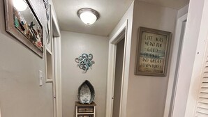 A hallway with a patterned rug, a decorative mirror, a small table with a mirror, and a motivational quote on the wall. - 2-bedroom house w/pool in the heart of old Homosassa! (Homosassa)
