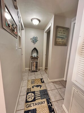 A hallway with a patterned rug, a decorative mirror, a small table with a mirror, and a motivational quote on the wall. - 2-bedroom house w/pool in the heart of old Homosassa! (Homosassa)