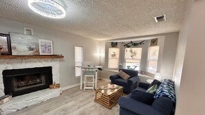 A living room with a fireplace, a blue sofa, a wooden coffee table, and a ceiling light fixture. - 2-bedroom house w/pool in the heart of old Homosassa! (Homosassa)