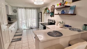 A modern kitchen with a central island, a refrigerator, and a dining area with chairs. - 2-bedroom house w/pool in the heart of old Homosassa! (Homosassa)