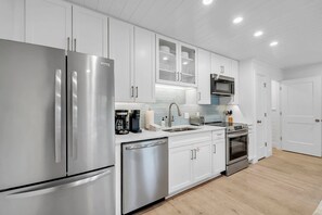 A modern kitchen with stainless steel appliances, white cabinetry, and a tiled backsplash. - Saltwater Society by Stay on 30a (Inlet Beach)