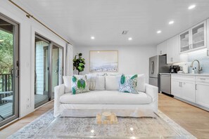 A modern living room with a white sofa, a coffee table, and a painting on the wall. - Saltwater Society by Stay on 30a (Inlet Beach)