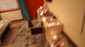Una habitación con piso alfombrado, una cama, una mesita de noche y un ventanal con cortinas.