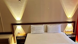 Una cama bien hecha con sábanas blancas, dos mesitas de noche con lámparas y un cabecero de madera.