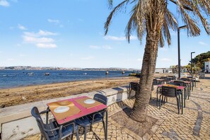 Un patio frente al mar con mesas y sillas, una palmera y vistas al océano.