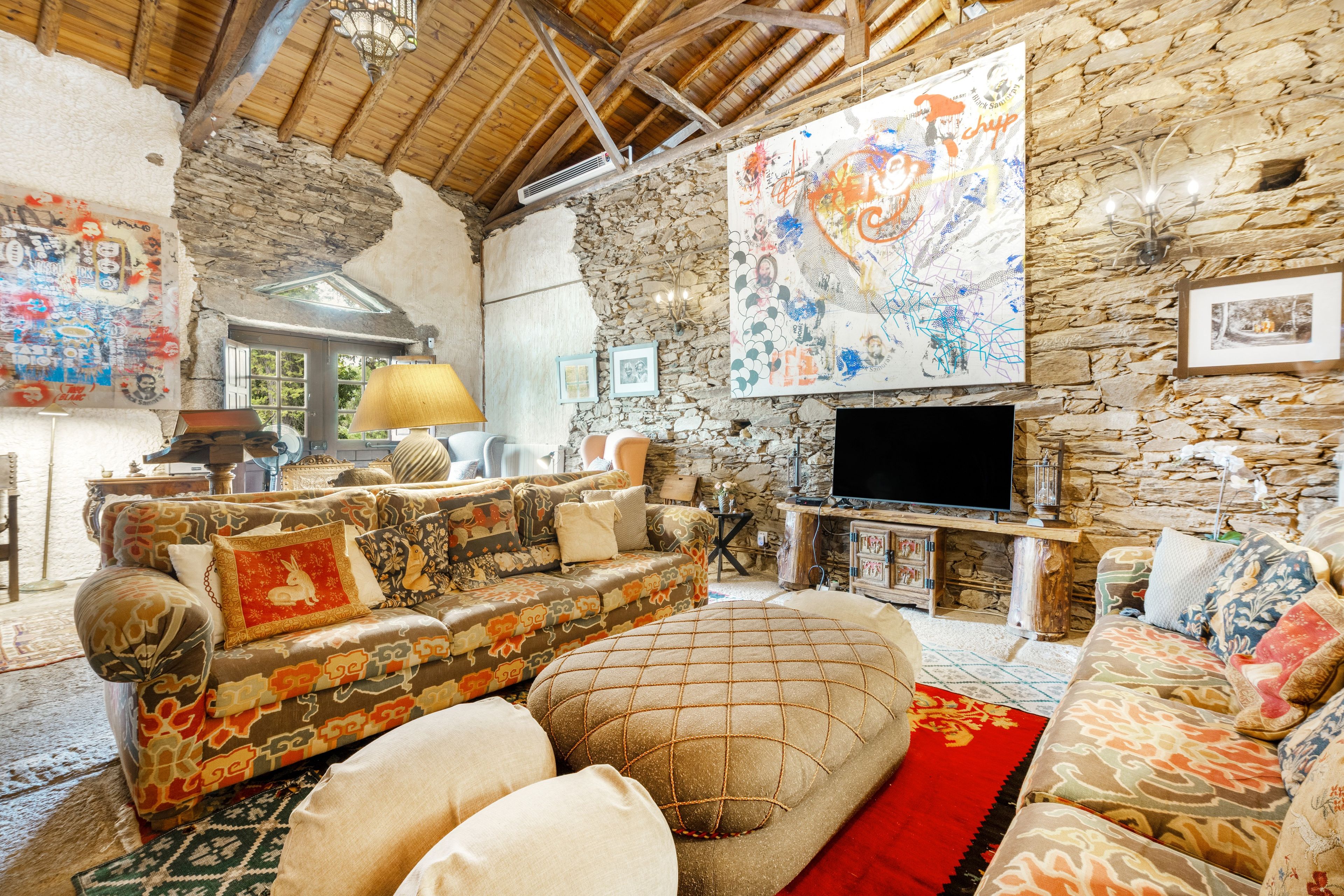 Un intérieur rustique avec un mur en pierre, un grand tableau abstrait, un ensemble de meubles de salon et un téléviseur.