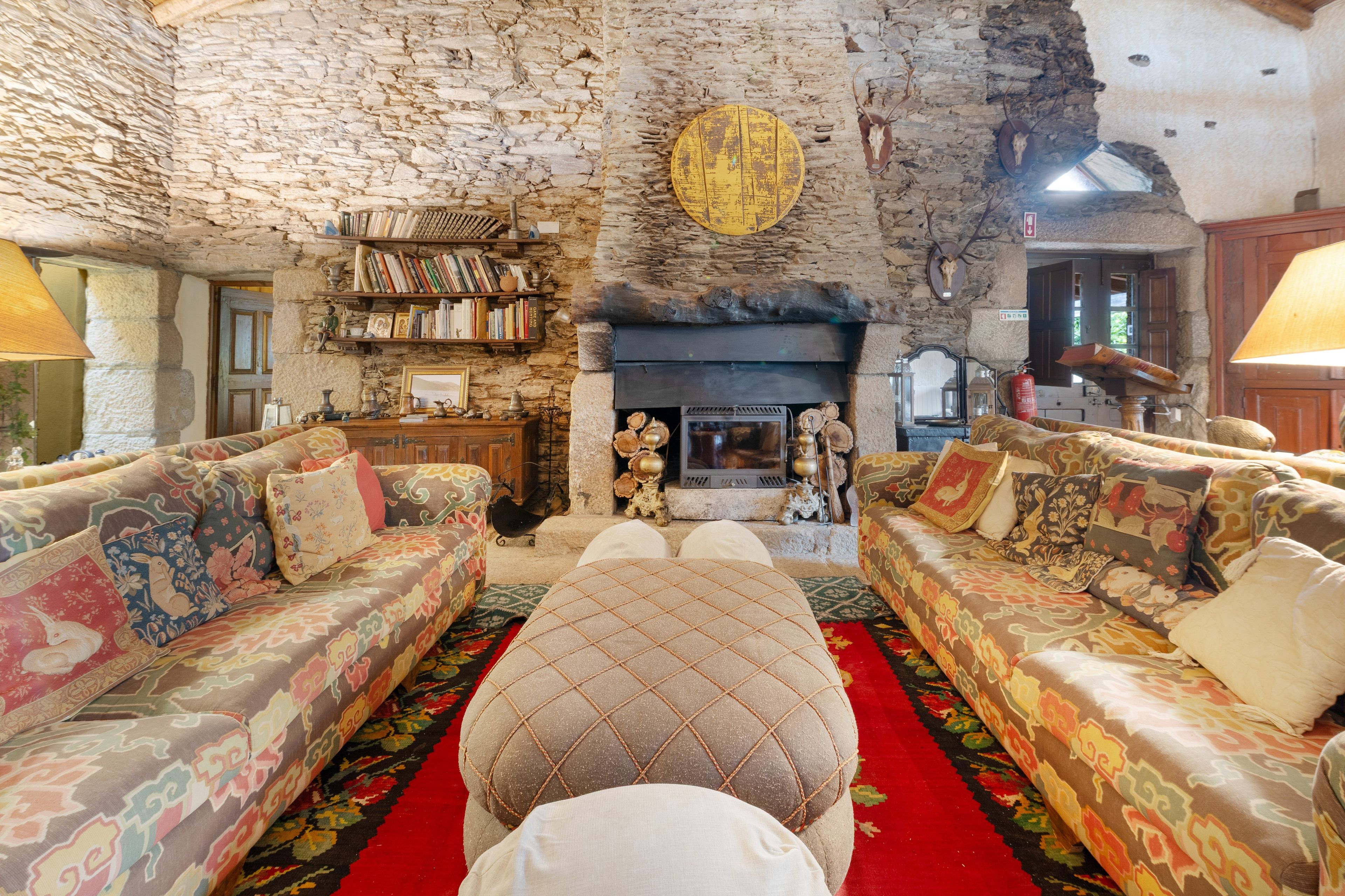 A rustic living room with stone walls, a fireplace, and patterned sofas.