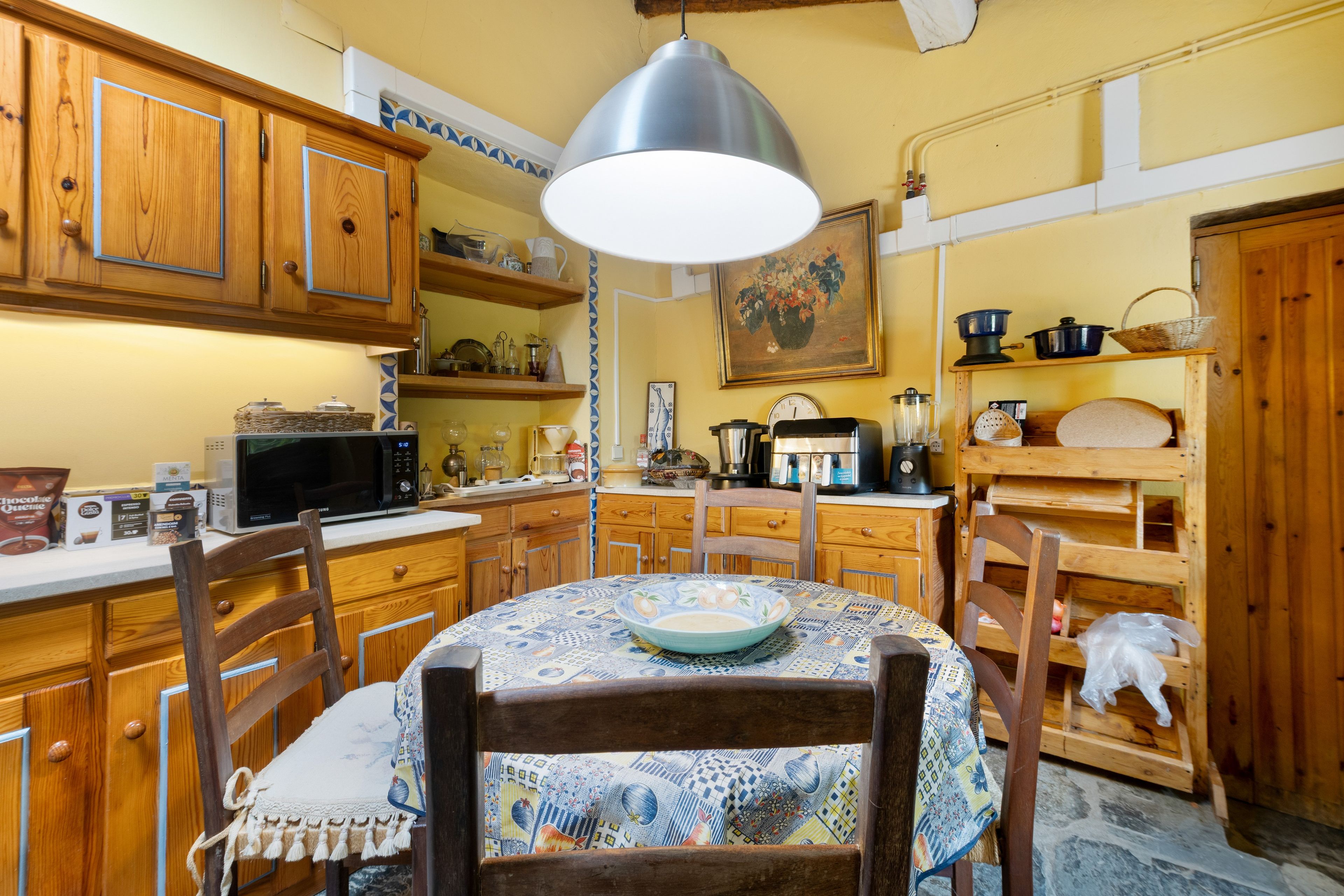 Una cocina con armarios de madera, microondas, cafetera y una mesa de comedor con sillas.