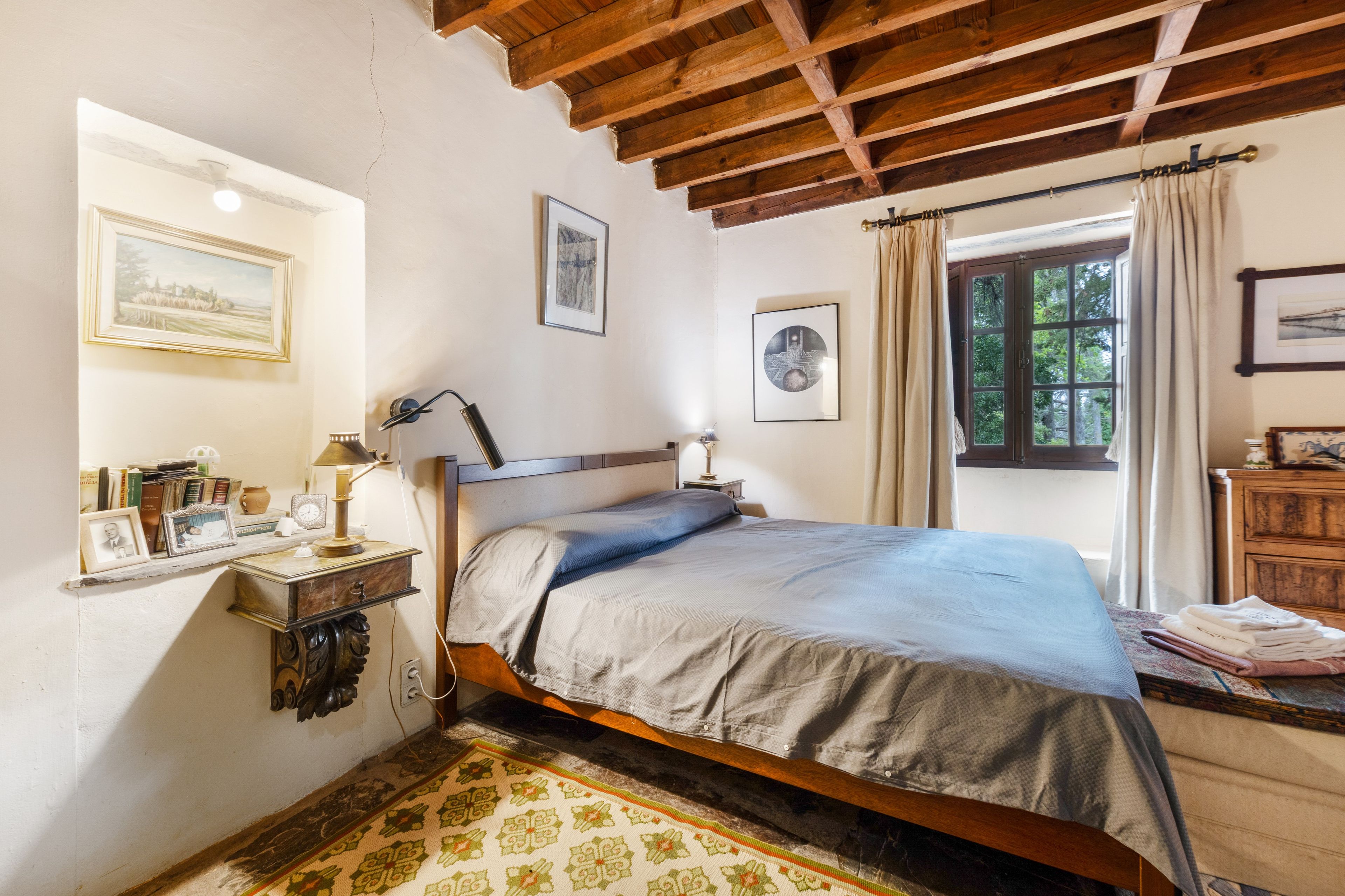 Una camera da letto con un letto di legno, un comodino con una lampada, una finestra con tende e una parete decorata con quadri.