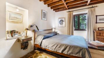 Una camera da letto con un letto di legno, un comodino con una lampada, una finestra con tende e una parete decorata con quadri.