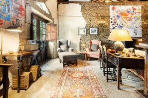 Una habitación acogedora con pared de piedra, alfombra estampada y una mezcla de muebles antiguos y modernos.