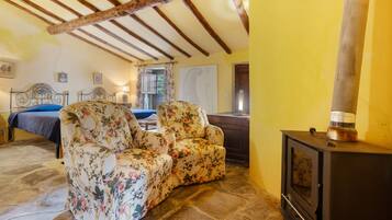 Una habitación con una cama, dos sillones florales, una mesa de madera y una chimenea.