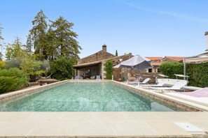 A swimming pool with lounge chairs and umbrellas, surrounded by trees and a stone building.