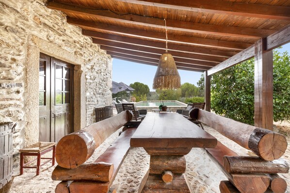 A rustic outdoor seating area with a stone wall, wooden beams, and a hanging light fixture.