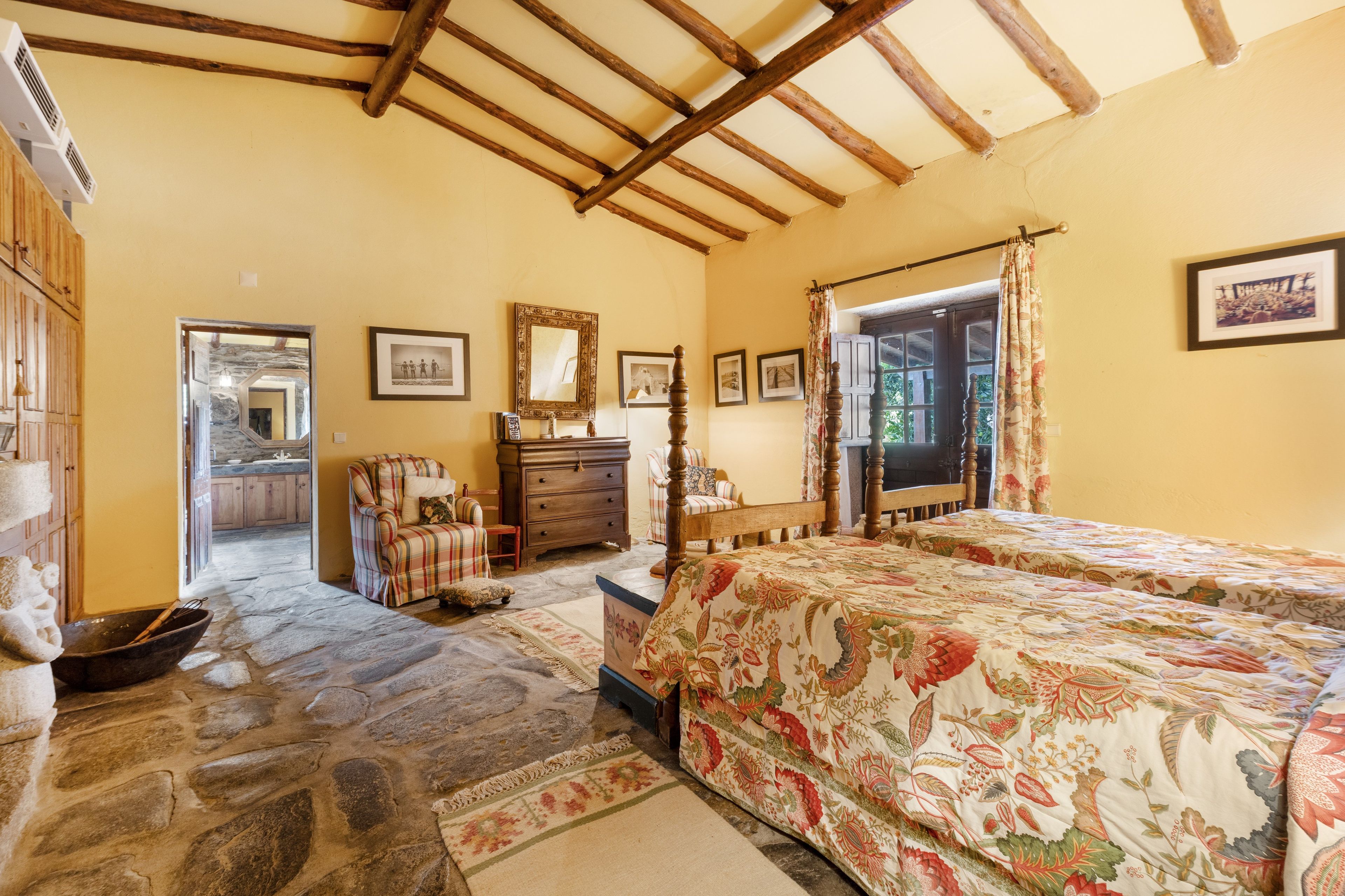 Un dormitorio con techo de madera, una cama con ropa de cama floral, un aparador y un espejo.