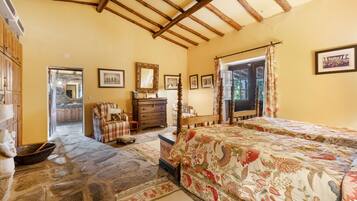 Un dormitorio con techo de madera, una cama con ropa de cama floral, un aparador y un espejo.